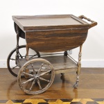Antigo carrinho de chá estilo inglês confeccionado em madeira nobre entalhada, com duas prateleiras sendo a superior articulável, pés, apoios e raios das rodas torneados. Med: 84 x 67 x 67cm