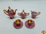 Miniatura de jogo de café com 5 peças em porcelana rosa com ouro. Medindo o bule 6,5cm de altura.