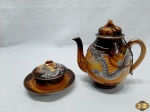 Jogo de manteigueira e bule em porcelana oriental com dragão em relevo. Medindo o bule 16cm de altura. A manteigueira possui um leve bicado na borda do prato.
