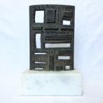 Antiga placa em bronze maciço, rematada com figuras e fendas retangulares. Base em mármore. Dimensões: 25 cm x 16 cm x 8 cm.