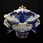 Antigo e belo pote com tampa em porcelana esmaltada, anos 50,  decorado com folhas de acanto e perolados em alto relevo. Modelo ostentando  4 pés curtos, ricamente decorados.Detalhes na cor azul Royal e ricos filetes pintados à Ouro 24 k. Exemplar de coleção e  em excelente estado de conservação. Numeração e selo de manufatura no fundo. Dimensões: 15 cm x 19 cm x 12 cm.