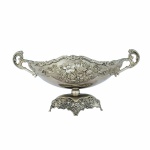 Suntuoso e antigo centro de mesa  no formato de navete em metal cinzelado e niquelado rematado com arabescos, flores e perolados. Base apoiada por 4 pés estilizados. Exemplar em excelente estado de conservação. Dimensões: 33 cm x 16 cm x 16 cm.