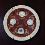 Prato em porcelana Oriental, fundo bordô com monogramas e realces pintados à Ouro. Ideal para colocar em portas ou paredes. Dimensões: 15,5 cm de diâmetro.