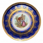 Exuberante Medalhão em fina porcelana, anos 50, na cor azul Royal com cena galante ao centro. Decorado no requinte Alemão, com belíssimos arabescos e filetes pintados à Ouro.Exemplar em excelente estado de conservação.Dimensões: 32 cm de diâmetro.