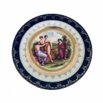 Epiag Czechoslovakia - Suntuoso Medalhão em fina porcelana, estilo neoclássico. Pintura ao centro com ninfas observando homem tocando Harpa.  Pintura Angelica Kauffman - Importante pintora neoclássica Suíça 1741 - 1807. Borda rematada com larga faixa azul cobalto, arabescos e estilizados pintados à Ouro. Exemplar raro e em perfeito estado de conservação. Dimensões: 25,5 cm diâmetro.