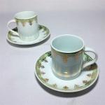 SCHMIDT - Par de xícaras e pires para café anos 50 em porcelana branca esmaltada, decoradas com faixa verde claro nas bordas e cascatas florais gravados à Ouro. Exemplares em perfeito estado de conservação. Dimensões: Xícaras 6 cm x 7 cm e pires 11 cm  diâmetro.