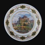 Belíssimo medalhão em porcelana decorado com imagem de Château, ladeada por  larga faixa  com detalhes de galerias e rosas. Filetes e estilizados rematados à Ouro. Dimensões: 30 cm diâmetro.
