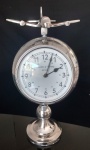 Relógio em alumínio escovado, sendo ele um globo terrestre, decorado com avião acima do globo. Medidas . 43x22 cm. Relógio a pilha e com a base descascando.