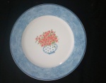 Elegante prato em porcelana Vista Alegre ao fundo com vaso e flores e bordas na cor  azul  -Diâmetro: 27 cm