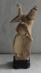 Escultura em resina representando homem oriental em pose dançante, sobre nuvem. Apoiado em base de resina negra com flores e símbolos esculpidos. Medida: 26,5cm de altura