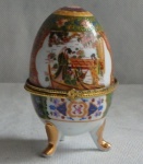 PORCELANA  - Lindo Ovo decorado com cenas orientais, ao gosto família rosa, apoiado sobre 3 pés folheado a ouro, ao centro anel em metal dourado. Alt.10 cm