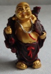 Pequena escultura oriental com figura de buda segurando leque e mochila nas costas, figura laqueada no tomo vermelho rubi e dourado. Alt.7 cm