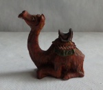 Escultura em resina de camelo descansando com montaria na corcova. Med. 9cm x 10cm