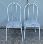 Duas cadeiras em metal branco ondular com assento almofadado com estampa azul e branca.