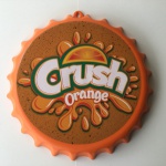 Arte promocional da CRUSH na forma de tampa de garrafa em plástico, medindo 28 cm de diâmetro.