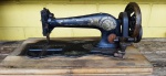 Antiga máquina de costura Singer a manivela sobre caixa de madeira, cor preta com detalhes em ouro, possui desgaste do tempo. Med.: 26 cm de altura