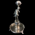 Paliteiro em prata batida, repuxada e cinzelada, representando mulher com globo. Marcas de ourives não identificado. Brasil, Séc. XIX. 15 cm de altura.