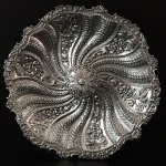 Salva de aparato no estilo D. José I, em prata batida, repuxada, fundida e cinzelada. Portugal. Séc. XIX. 1.050 Kg. 40 cm de diâmetro.