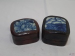 Lote de 2 caixas em madeira com tampa em porcelana. Medindo a maior 9cm x 9cm x 6cm de altura.