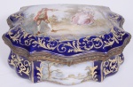 França Séc XIX / XX, Caixa em porcelana de Sévres, na cor azul cobalto, com detalhes em pintura dourada, decorada com cena galante assinada por W.Gravey, medindo 13 cm de altura, 18 cm de profundidade e 25 cm de comprimento.