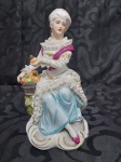 Figura de porcelana representando vendedora de frutas com aproximadamente 25 cm de altura e em bom estado de conservação.