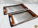 Lote de 2 bandejas retangulares em aço inox com alça em madeira. Medindo a maior 45,5cm x 25,5cm e a menor 39cm x 20,5cm.