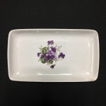 SCHMIDT - Travessa em fina porcelana, anos 60 decorada com arranjo de Violetas ao centro. Exemplar em perfeito estado. Dimensões: 17,5 cm x 10,5 cm.