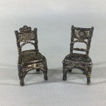 Delicada miniatura de par de cadeiras em metal cinzelado banhado à prata. Exemplares antigos em excelente estado. Dimensões: 5 cm.
