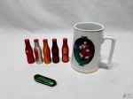 Lote diverso, composto de 5 mini garrafas da Coca Cola em aluminio, 1 canivete com 3 funções e caneca com motivo natalino da Coca Cola. Medindo a caneca em porcelana 12cm de altura.