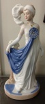 Estatueta em porcelana. Dama em trajes de gala. Med. 30 x 16 x 11 cm.