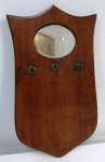 Porta chave no formato de escudo em madeira maciça com pequeno espelho bisotado oval. Mede: 40x21 cm