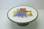 FAIANÇA EUROPÉIA - Linda prato alto para bolo em faiança, com base cônica e aro em metal. Faiança decorada com jarra e frutos. Med. 13x32 cm.