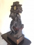 RELÓGIO - Bela escultura em madeira, ricamente entalhada, representando Homem sobre tronco, carregando suporte de relógio nas costas. Máquina de relógio a pilha. Sem funcionamento aparente. Escultura assinada.