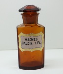 Antigos frasco de farmácia em cristal tonalidade âmbar ornamentado com as inscrições MAGNES CALCIN LIV. com rótulo opalinado branco filetado em ouro. França. Final do século XIX. 21 cm. Desgastes e marcas naturais do tempo.