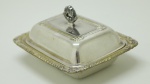 METAL ESPESSURADO A PRATA - Pequena manteigueira em metal espessurada a prata, ricamente decorada e com recipiente interno em demi cristal. Med. 6x12x9 cm.