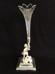 METAL ESPESSURADO A PRATA - Delicada floreira em base em metal espessurado a prata, representando infante sustentando soliflor em cristal, ricamente lapidado e gravado, datado de 1882. Med. 23x8x8 cm.