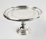 ELEGANTE SALVA DE ESMOLAS EM PRATA DE LEI BATIDA E CINZELADA COM MARCAS PARA CIDADE DO PORTO (P COROADO) E PRATEIRO MJPS REFERENCIADO POR MOITINHO COMO MARCA P480 (PAG 276) E DATÁVEL A PARTIR DE 1860. BORDA DECORADA POR SUCESSIVOS ANÉIS CONCÊNTRICOS. PLANO POSSUI LINDA GUIRLANDA VEGETALISTA COM FLORES E RAMAGENS QUE EMOLDURAM REPRESENTAÇÃO DO DIVINO ESPÍRITO SANTO (POMBA). FUSTE EM BALAÚSTRE. A BASE CIRCULAR APRESENTA-SE EM PLATEAU CONSTITUIDO DE ANÉIS CONCENTRICOS COM DIÂMETRO CRESCENTE, 22 centímetros de diâmetro e 14 centímetros de altura. FUSTE É ROSQUEÁVEL PARA LIBERAR A PARTE SUPERIOR DA SALVA. NOTA: As salvas de esmola faziam comumente parte do cotidiano da cristandade até o sec. XIX. Cada irmandade tinha a sua que ficava sobre o altar da irmandade nas igrejas ou era conduzida nas ruas pelos irmãos que coletavam esmolas. Há um texto de Machado de Assis, chamado O Dístico publicado originalmente no periódico. A Quinzena, nº. 7, 1º. de julho de 1886 relata o uso cotidiano dessa alfaia: Já lá vão vinte anos, ou ainda vinte e dois. Foi na Rua de S. José, entre onze horas e meio-dia. Vi a alguma distância parado um homem de opa, creio que verde, mas podia ser encarnada. Opa e salva de prata, pedinte de alguma irmandade, que era das Almas ou do Santíssimo Sacramento. Tal encontro era muito comum naqueles anos, tão comum que não me chamaria a atenção, se não fossem duas circunstâncias especiais.... Muitas vezes as salvas de esmola trazem indicação da irmandade a que pertencem seja por simbologia ou por escrita.