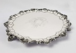 prata de lei vitoriana - magnífica salva em prata de lei com marcas para cidade de londres e letra data para o ano de 1885 (período vitoriano). elegante estilo georgiano tem a borda recortada e está assente sobre tres elegantes pés com feitio de escudelas. ao centro lindo trabalho em guilloche com guirlanda vegetalista. a guirlanda é sustentada por dois belos querubins, um do lado esquerdo e o outro do direito. um dos querubins segura uma coroa de louros. no alto da guirlanda também é representado um tridente. inglaterra, 1885, 32 cm de diametro
