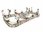 DRESDEN  PALACIANO CENTRO DE MESA EM PORCELANA DA MANUFATURA DRESDEN, COMPOSTO POR FLOREIDAS DIVERSAS PERMINDO DIFERENTES CONFIGURAÇÕES. SÃO TRINTA PEÇAS ENTRE ESCULTURAS (QUERUBINS), ÂNFORAS E JARDINEIRAS. SÃO DECORADAS COM GUIRLANDAS FLORAIS E REMATADAS EM OURO. AS ÂNFORAS E ESCULUTURAS SÃO ELEVADAS POR ALTAS BASES RETANGULARES. COM ESSA CONFIGURAÇÃO DE MONTAGEM TEM 140 CM X 65 CM. ALEMANHA, SEC. XIX/XX. 33 CM DE ALTURA (ESCULTURAS DOS QUERUBINS)NOTA: Centros de mesa ricamente decorados com prata, cobre ou bronze eram parte integrante da decoração de mesa de grandes refeições durante o século XIX. A prática de decorar o centro das mesas da sala de jantar com obras de arte remonta a séculos. Por exemplo, durante os séculos XIV e XV, as sobremesas muitas vezes assumiam a aparência de uma peça central, mas foi durante o século XVII que o uso de uma peça central artística se tornou comum, associando objetos decorativos com iluminação e buquês de flores opulentos. Esses objetos costumavam ser exibidos em uma grande bandeja composta de uma ou mais peças que às vezes eram espelhadas e às vezes colocadas em uma estrutura decorativa.