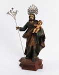 SÃO JOSÉ DE BOTAS  BELA ESCULTURA EM MADEIRA POLICROMADA REPRESENTANDO SÃO JOSÉ COM MENINO JESUS. RESPLENDOR E LÍRIO EM PRATA DE LEI. BRASIL, SEC. XIX. 28 CM DE ALTURA (SEM CONSIDERAR O TAMANHO DO RESPLENDOR)NOTA: São José de Botas é uma invocação típica do Brasil colonial. Para alguns historiadores, está associada à figura dos bandeirantes que marchavam para o interior com suas grandes botas de cano alto. São José de Botas alude ao desterro para o Egito que a Sagrada Família se impôs para fugir da fúria do Rei Herodes. A origem do lírio de São José como atributo tem algumas teorias: A primeira e a mais difundida, é a de que ele representa a pureza de São José, porque Maria concebeu sem pecado ou conjunção carnal. Existem entretanto outras vertentes que dizem que José ainda sem conhecer Maria foi a uma festa religiosa no templo e levava um cajado pelo caminho para proteger-se no percurso e servir como suporte. Ao deparar-se com Maria seu cajado teria florescido imediatamente com belos cachos de lírios brancos. Finalmente há uma versão teológica que defende que as palavras dos profetas do velho testamento apontavam para São José em suas profecias. Vide Isaias 11:1-2 Eis que um ramo surgirá do tronco de Jessé e das suas raízes um rebento brotará. O Espírito de Yahweh, o SENHOR, repousará sobre ele, o Espírito que dá sabedoria e entendimento, o Espírito que traz conselho e poder, o Espírito que proporciona o verdadeiro saber, o amor e o temor do SENHOR.