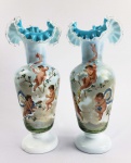 LINDO PAR DE VASOS EM OPALINA DECORADOS COM ESMALTES REPRESENTANDO FIGURAS DE QUERUBINS  EM DUAS CENAS DISTINTAS EM UM DELES TRÊS QUERUBINS ESTÃO EM TORNO DE UM NINHO DE PASSAROS EM UMA ÁRVORE FLORIDA. NOTA-SE PAISAGEM COM RELVA E MONTANHAS AO FUNDO. NO OUTRO TRÊS QUERUBINS EM SEUS FOLGUEDOS. BORDAS TIOTADAS EM DEBRUM. FRANÇA, SEC. XIX. 33 CM DE ALTURA.