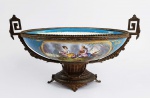 SEVRES  - MAGNÍFICO CENTRO DE MESA DE GRANDE DIMENSÃO EM PORCELANA COM GUARNIÇÕES EM BRONZE ORMOLU. FUNDO NA TONALIDADE AZUL CELESTE DECORADO COM RESERVAS DE UM LADO FLORAIS E DE OUTRO CENA IDÍLICA COM TOCADOR DE MUSETTE DE COUR (GAITA DE FOLES FRANCESA) ACOMPANHADO POR UMA DAMA EM PAISAGEM LACUSTRE COM CASA AO FUNDO. PROFUSAMENTE REMATADO EM OURO. O INTERIOR TEM BARRADO EM AZUL, DELIMATANDO COM GUIRLANDA EM OURO A CALDEIRA NA TONALIDADE BRANCA PROFUSAMENTE DECORADA COM FLORES EM GRANDE GUIRLANDA. PEÇA BELÍSSIMA! ESTILO E ÉPOCA IMPÉRIO. FRANÇA, DEC. 1860. 45 CM DE COMPRIMENTO.