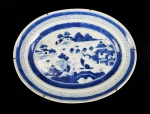 CIA DAS INDIAS - CANTÃO BELA TRAVESSA DE FEITIO OVAL CONSTRUÍDA EM PORCELANA UNDERGLAZE DO PERÍODO QIANLONG (1736-1795). BORDA COM BARRADOS EM AZUL FORMADOS POR FIGURAS GEOMÉTRICAS. RESERVA COM CENAS LACUSTRES, COM BARCOS, PONTE E PAGODES. CHINA, SEC. XVIII. 28 CM DE COMPRIMENTO.