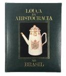 LOUÇA DA ARISTOCRACIA DO BRASIL POR JENNY DREYFUS - RARA E MAIS IMPORTANTE OBRA REFERENCIAL DA LOUÇA DOS TITULARES BRASILEIROS. Luxuosa edição, em papel couché, profusamente ilustrada com centenas de fotografias, na sua maioria a cores, de importantes e raras peças de porcelana, com a devida descrição pormenorizada, acompanhada da indicação da época de produção e da biografia resumida dos titulares a quem as peças pertenceram. Notável subsídio para o estudo da história social brasileira, com larga pesquisa dos serviços dos nobres do Império, das suas louças brasonadas, monogramadas ou simplesmente sem marcas e identificadas pelos seus descendentes, além do estudo das importantes baixelas da família imperial reinante e outros governantes do aparelho colonial, como vice-reis, governadores, capitães - generais e titulares portugueses que no Brasil permaneceram. Bom exemplar. Capa ilustrada com uma peça em porcelana que ostenta as armas de D. Pedro I, Imperador do Brasil, e IV de Portugal.. Rio de Janeiro. Monteiro Soares Editores e Livreiros. 1982. In -4º de 349 págs.