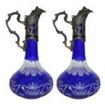 Par de decanters em cristal europeu, sendo o bojo em cristal de formato piriforme, ornamentado com facetas e lapidações em camada azul cobalto sobre incolor. Rematado com bocal em "pewter" fundido, cinzeladado e fenestrado. Europa. Início do século XX. 32 cm.