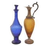Lote constando de duas peças, sendo: A) Decanter em cristal na cor âmbar com bojo lapidado e alças recurvas. 39.5 x 10 cm. B) Garrafa em cristal na cor azul. Bojo lapidado e base circular. 36.5 x 11 cm  tampa e bocal com bicado). Pertenceu ao Espólio de Vitória Dib Bachour.