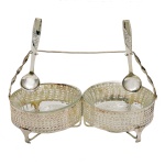 Conjunto de porta petiscos com suas colheres em metal prateado. Base circular e vazada, apoiada sobre três pés. Parte superior com apoios para as colheres. Pertenceu ao Espólio de Vitória Dib Bachour.
