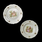Lote constando de dois pratos de porcelana polonesa. Fundo de superfície branca com cena de casais em jardim. Borda ondulada com reservas de bouquet florais. 24 cm e 22 cm. Marcas da manufatura no fundo Warbrzygh, Made in Poland. Pertenceu ao Espólio de Vitória Dib Bachour.