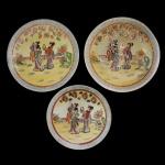Conjunto de três pratos de porcelana japonesa. Fundo de superfície amarela com personagens em jardim. Borda com friso na cor azul. No fundo a marca Wakamizu. (30 cm e 25,5 cm). Pertenceu ao Espólio de Vitória Dib Bachour.