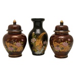Conjunto de três peças de porcelana japonesa, constando de:  A) Vaso com superfície preta apresentando decoração com pavões. 12 cm. B) Par de potiches com tampa de porcelana na cor vinho com pavões. 11 cm. Pertenceu ao Espólio de Vitória Dib Bachour.